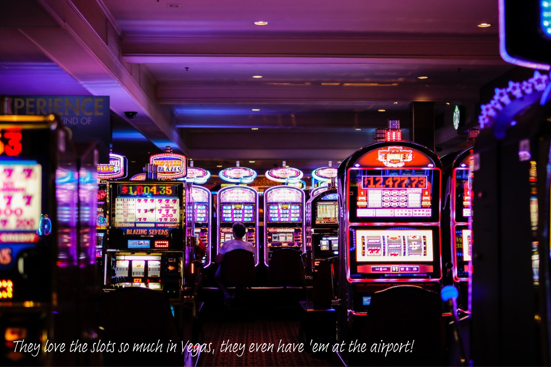 The inside of a casino, dark, with the glow of rows of slot machines.