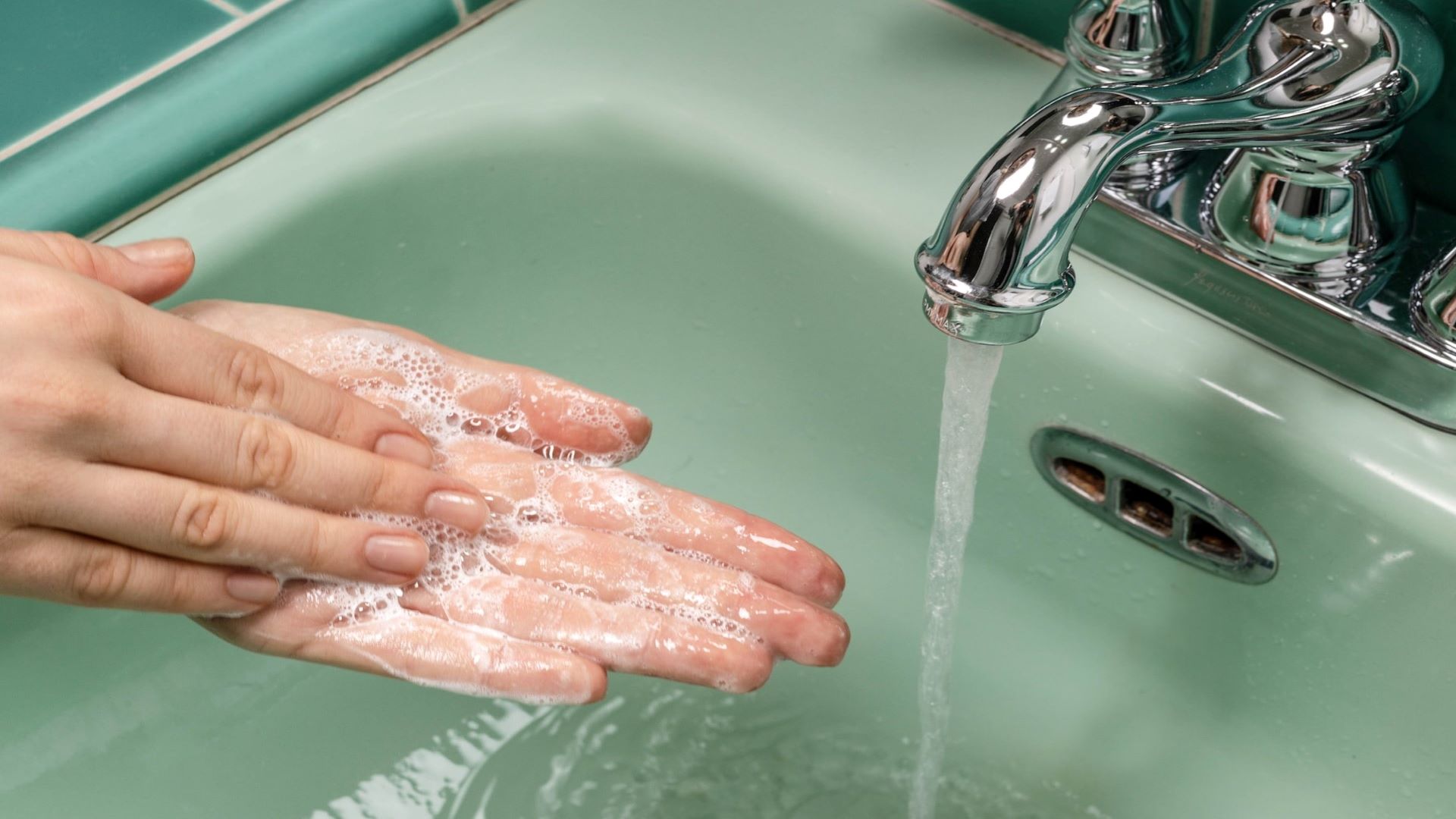 Cleanser being lathered in a pair of hands in a green sink under running water.