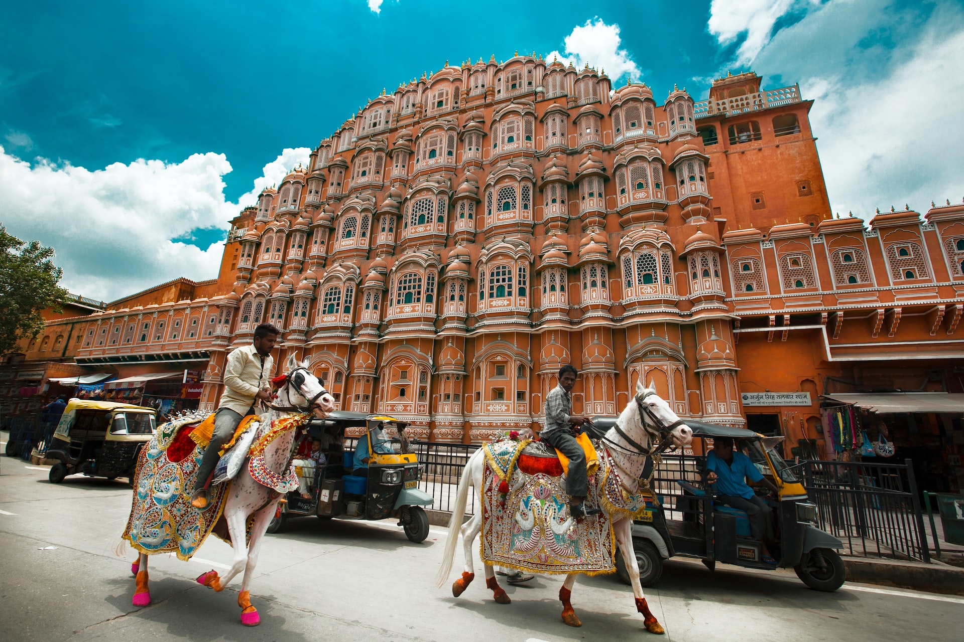 An image of a street scene in India, with Tuktuks in background and men riding horses in foreground.