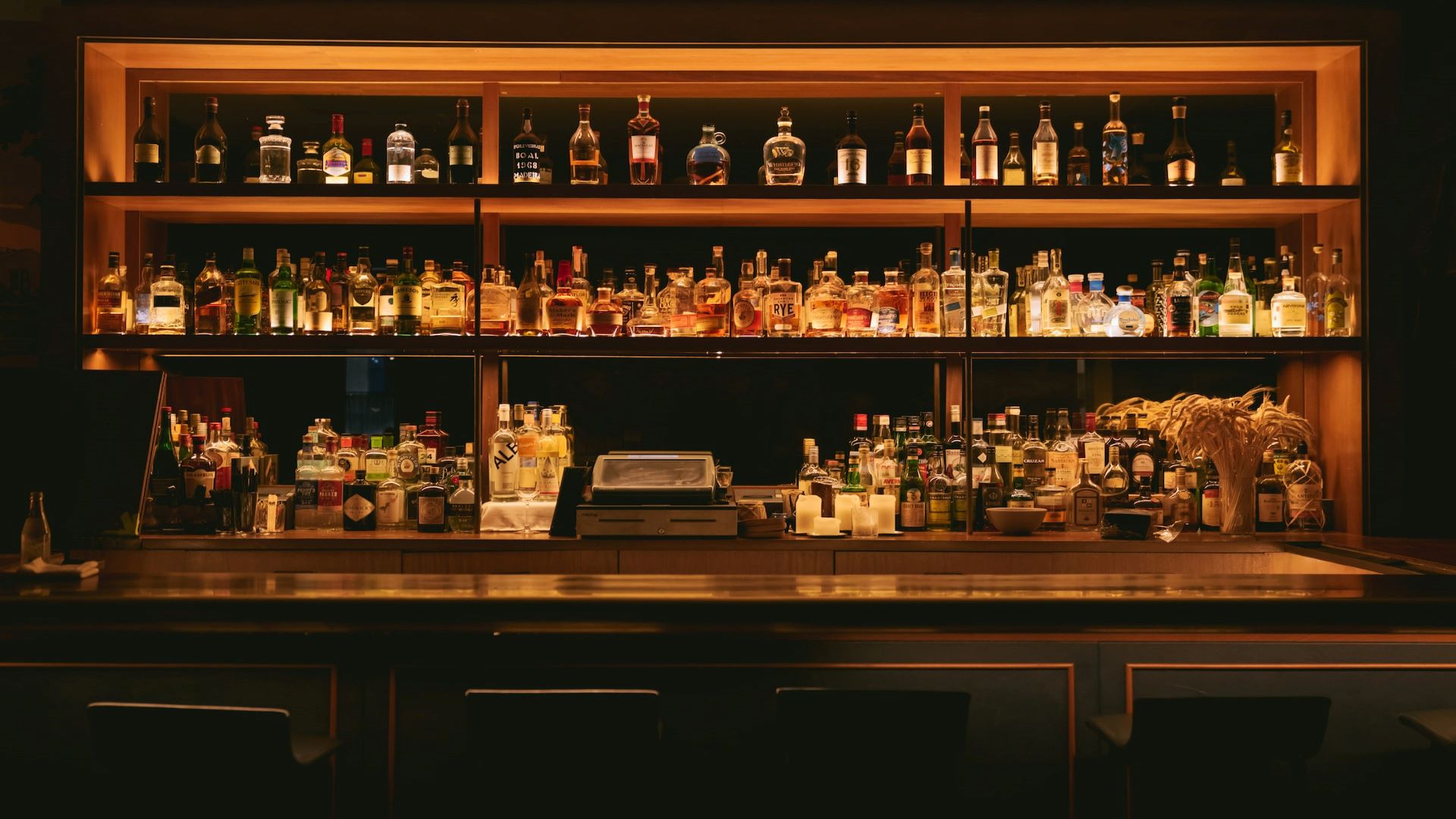 A bar, softly lit, with a row of bottles in the back.