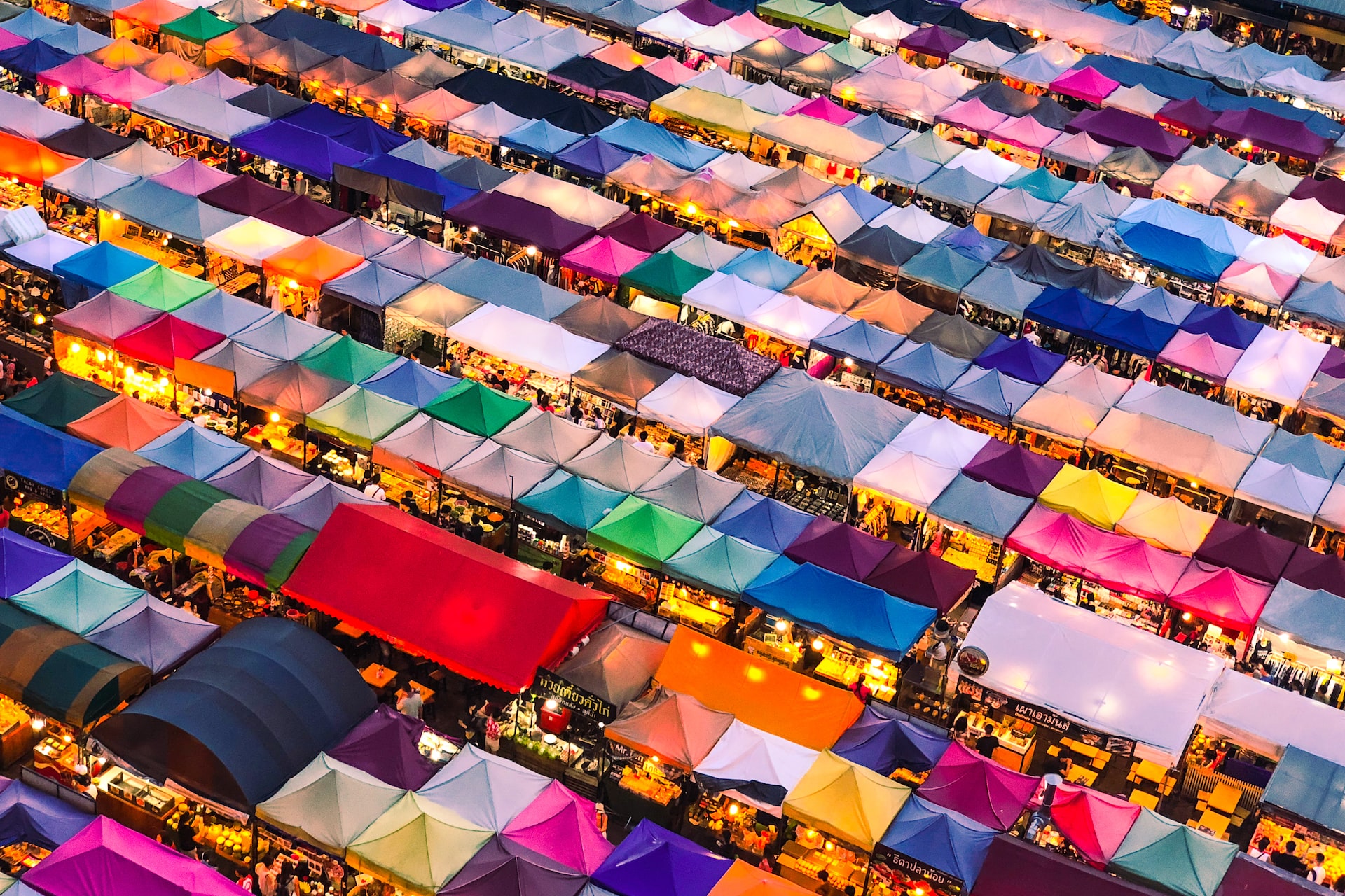 A bird's eye view of a market scene in Thailand; a patchwork of bright coloured stall coverings.
