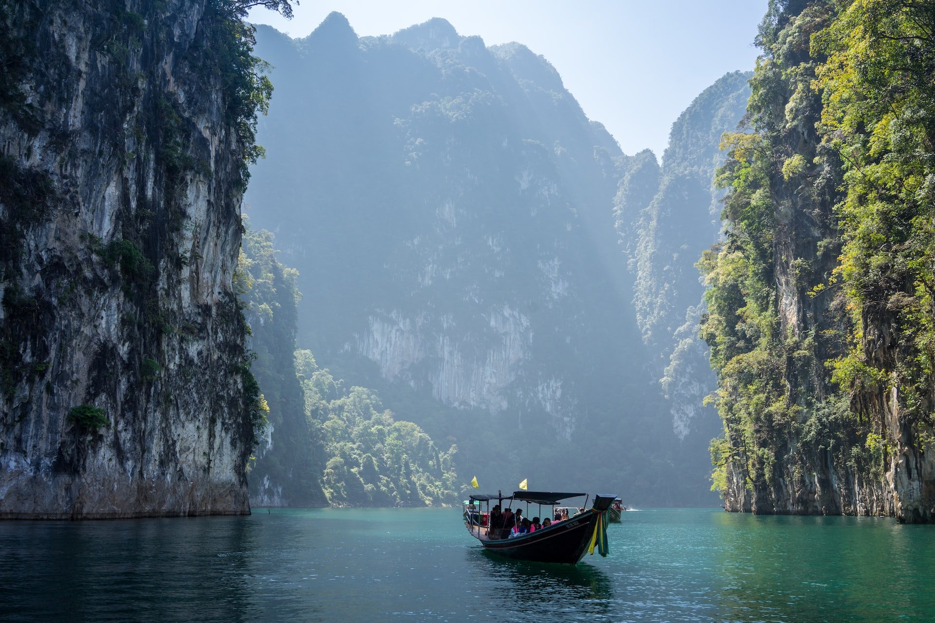 A boat floats on the water between two looming cliff faces in Khao Sok National Park, Khlong Sok, Thailand.