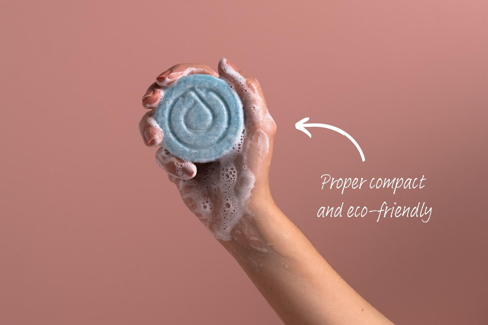 Hand holding a solid shampoo bar, with handwriting pointing to it saying, "Proper compact and eco-friendly."