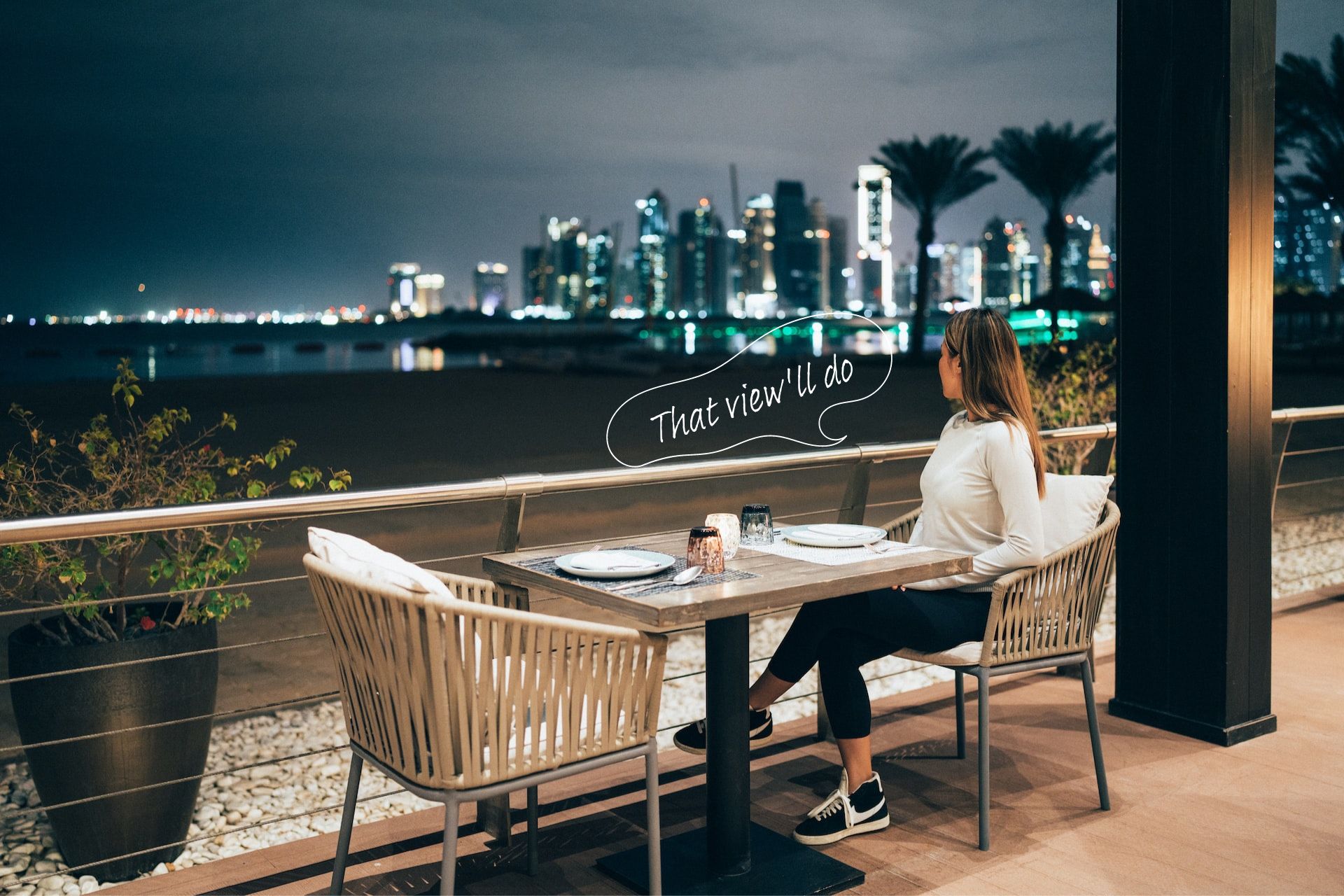 A woman looks at the skyline of Doha at night.