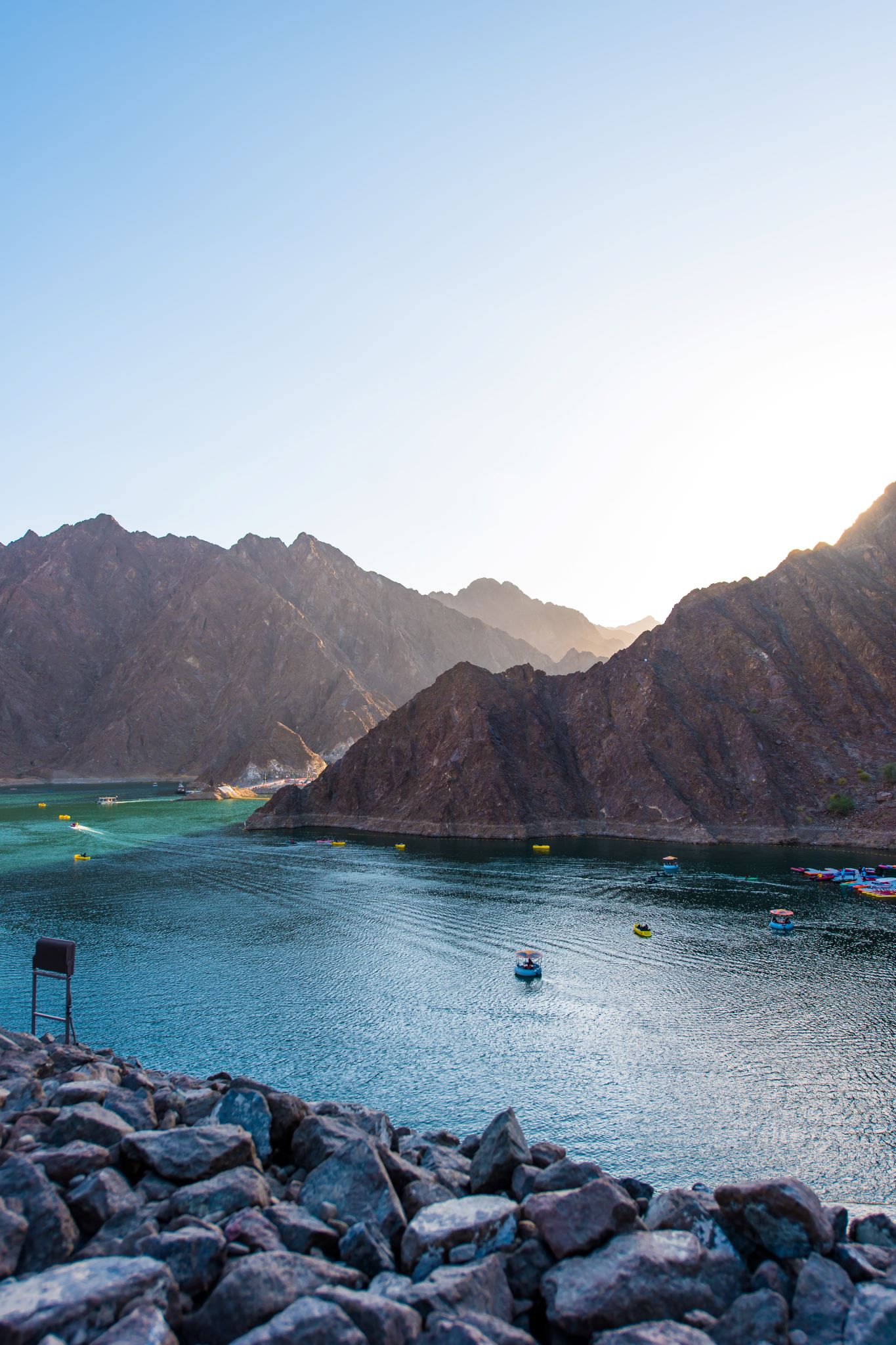 A boat sits on a blue Hatta Lake, the mountains soaring in the background.