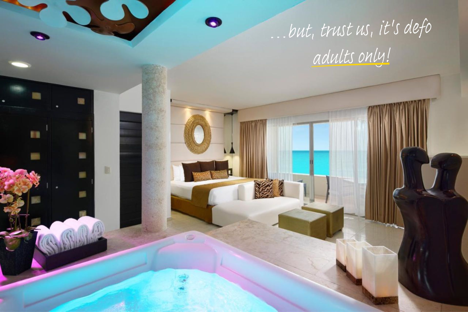 The Jacuzzi Room Ocean View at Desire Resort Cancun. A 4 person jacuzzi sits in one corner of the room, a large bed in the other, opposite a sculpture of two people embracing.