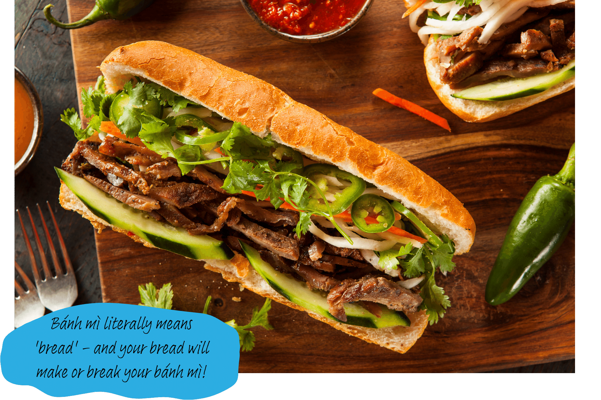 A bahn mi sandwich sits on a wooden chopping board, surrounded by various ingredients used in the making of it, including green and red peppers.