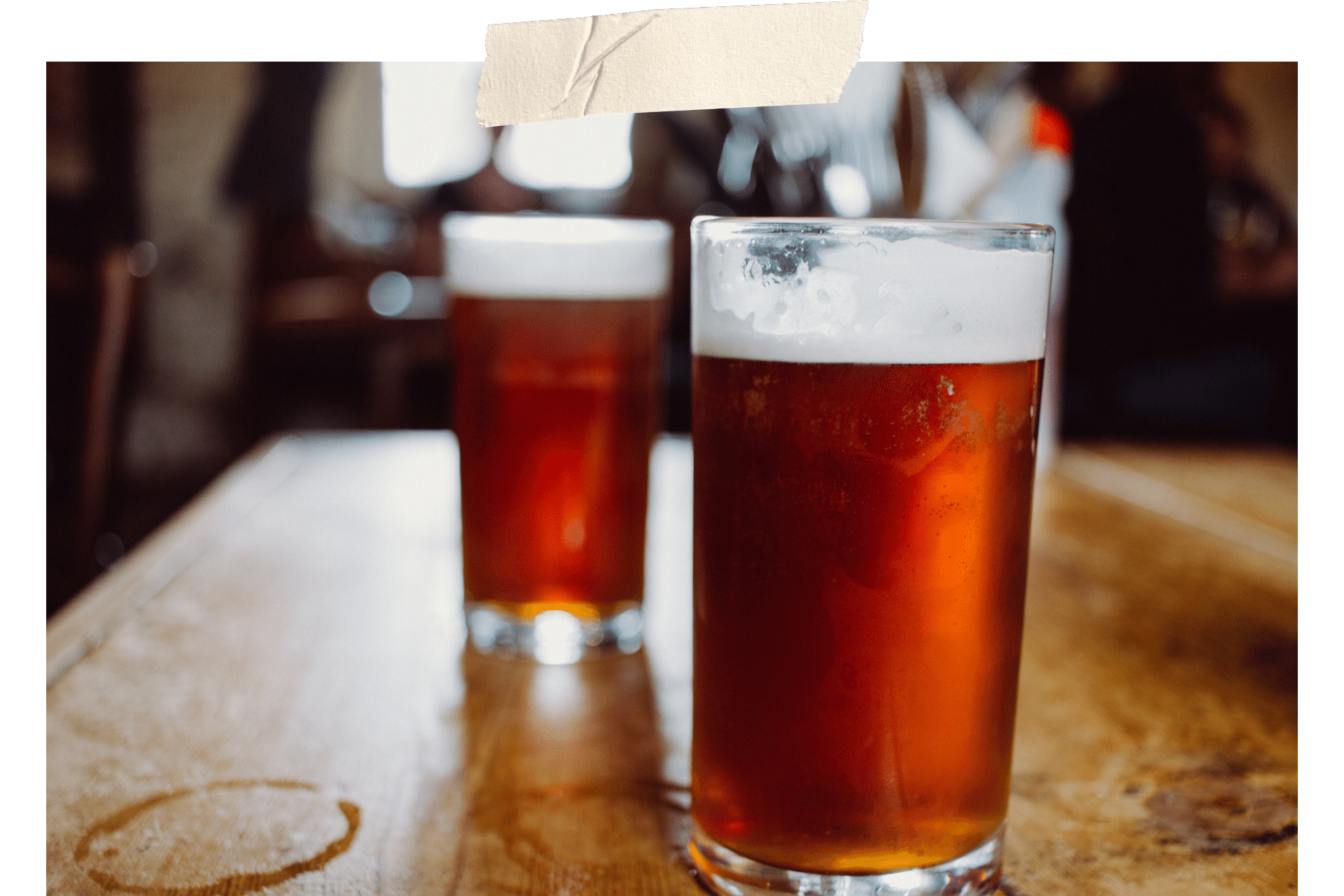 Image shows two pints of ale on a plain wooden table.