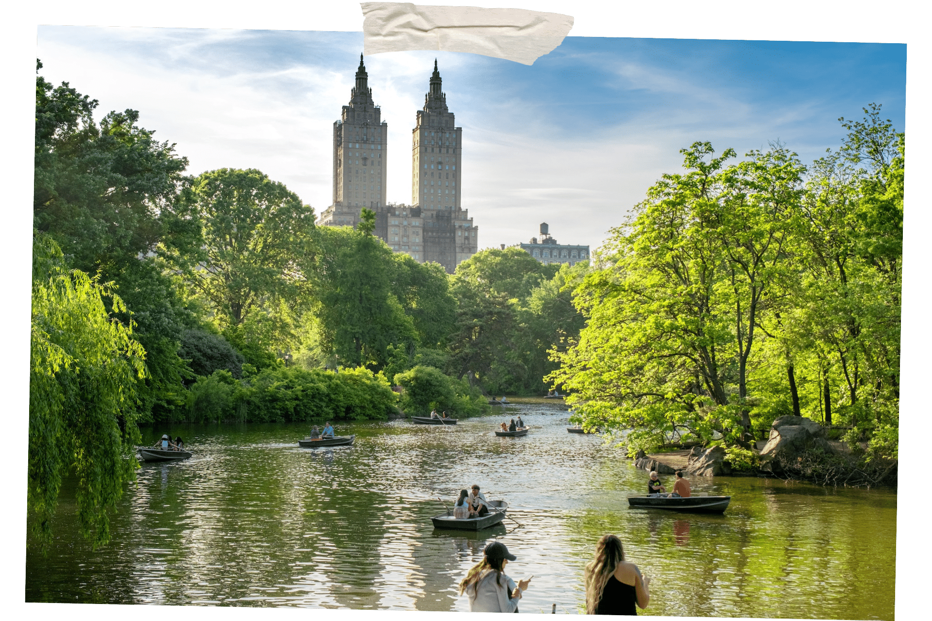 Picture shows boaters on the lake in Central Park, trees lining the bank, and high rises to the distance. Central Park is one of 8 great things to do outside in NYC.