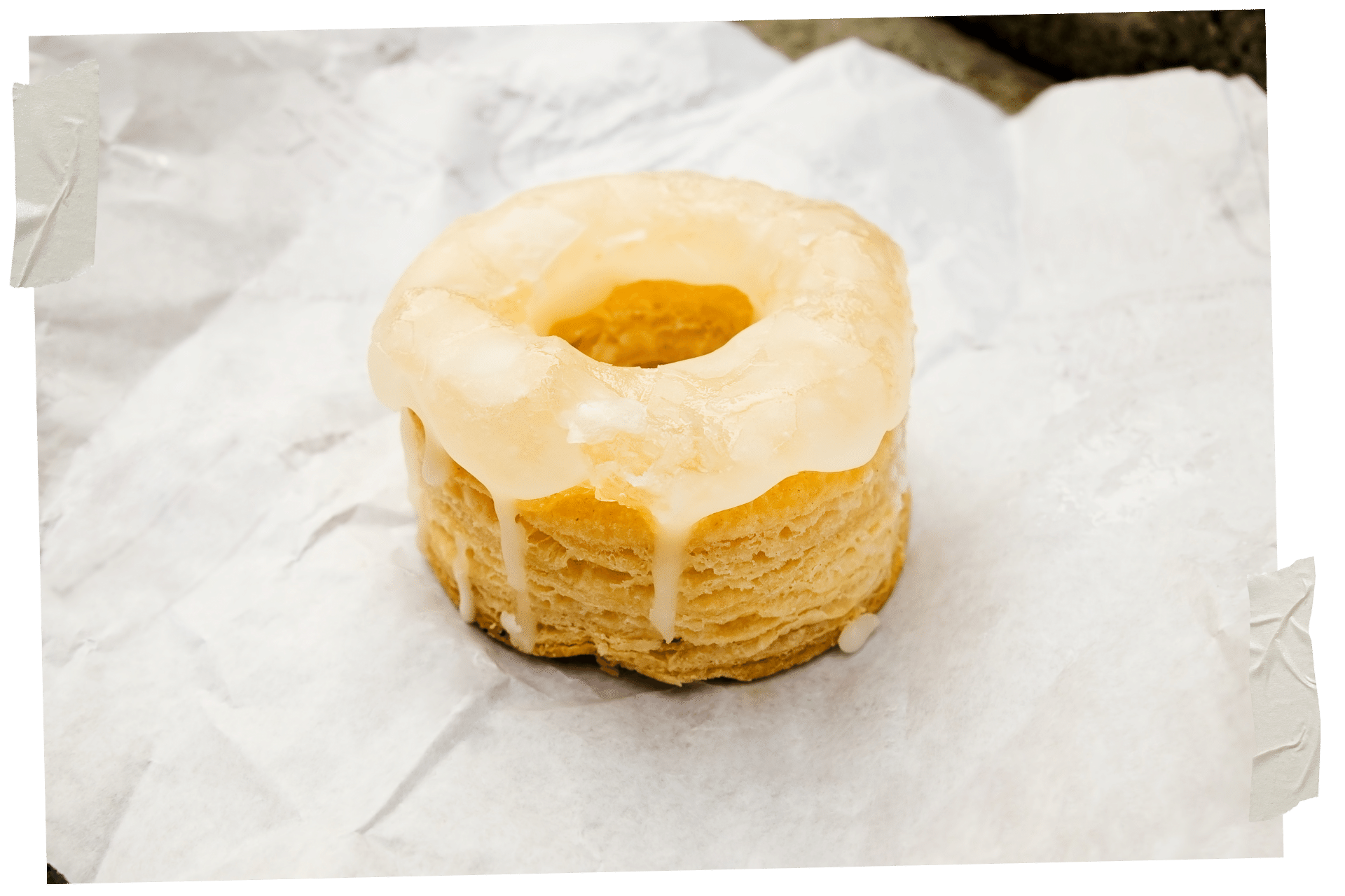 When it comes to New York for Foodies, you need to try a cronut. Pictured is a cronut - a mix between a croissant and a donut, on a piece of white tissue paper and with a pale yellow icing on top, dropping down the side.